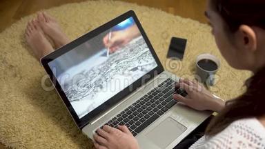 一位女士坐在地毯上的家里，看着屏幕上有艺术<strong>素描视频</strong>的笔记本电脑